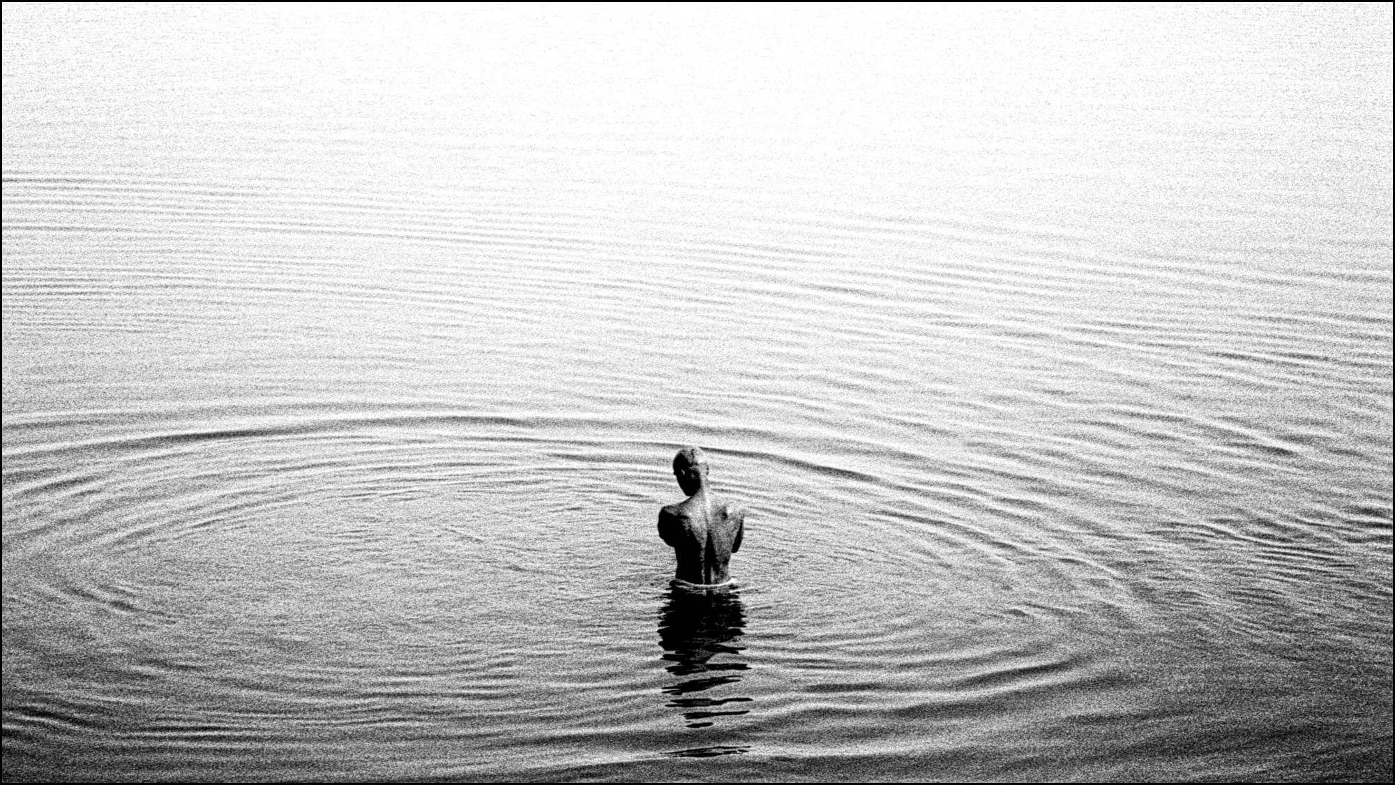 Un uomo immerso fino alla cintola nel fiume Gange a Varanasi in India. Fotografia in bianco e nero