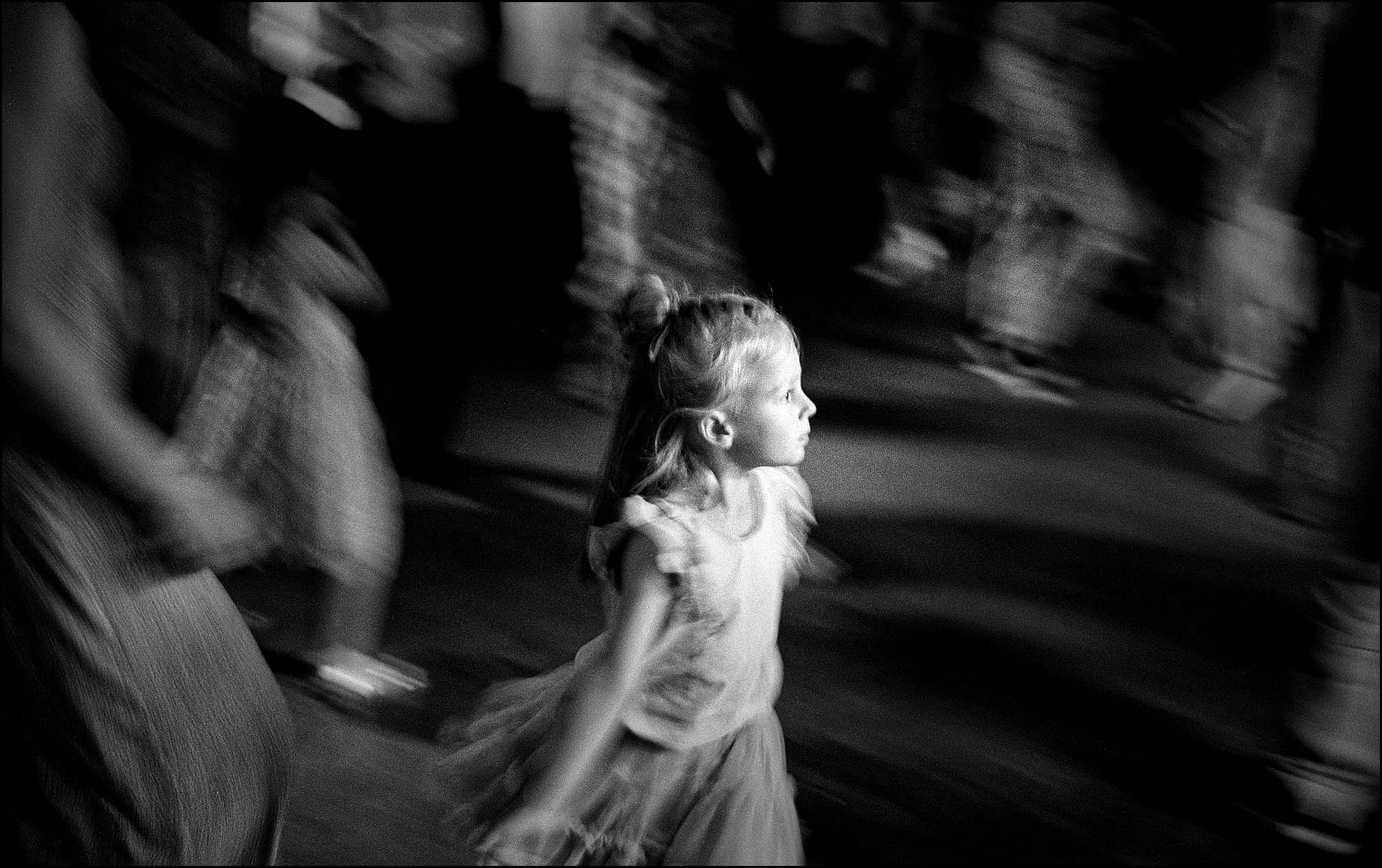 Una bambina che balla e altre persone sullo sfondo, in movimento. Fotografia in bianco e nero