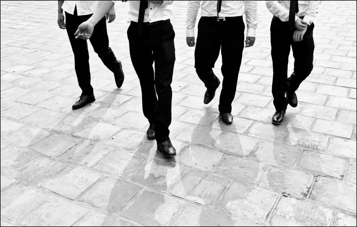 Quattro uomini ben vestiti avanzano in gruppo. Fotografia in bianco e nero.