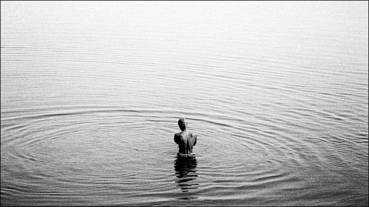 Un uomo immerso fino alla cintola nel fiume Gange. Fotografia in bianco e nero