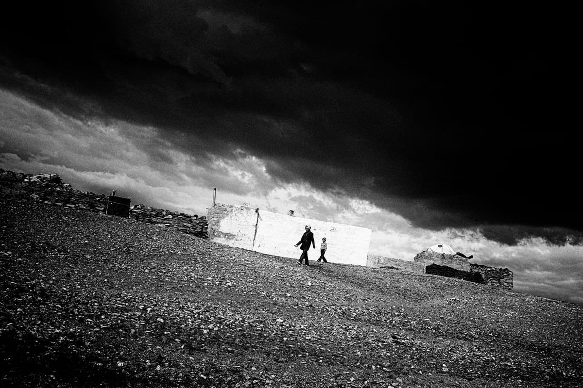 Due persone camminano sotto un cielo carico di pioggia. Fotografia in bianco e nero